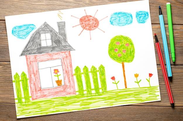 Дом забор цветы и яблоня детский рисунок на бумаге деревянный стол фломастерами