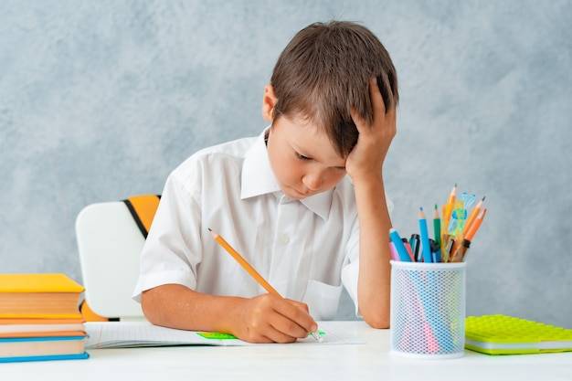 Снова в школу счастливый улыбающийся ученик рисует за партой школьник решает домашнее задание мальчик из эл