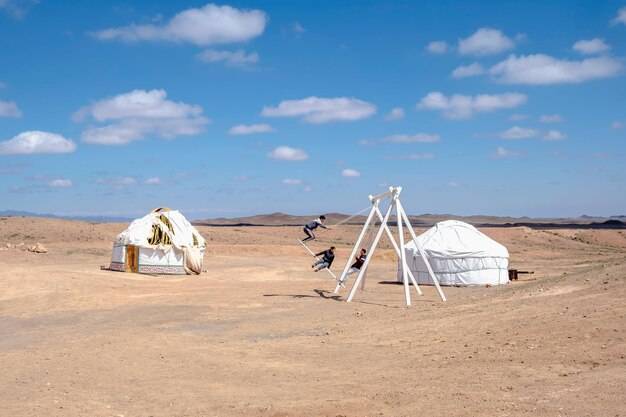 Белые юрты в степи дети катаются на больших качелях казахстан традиционное жилище кочевников