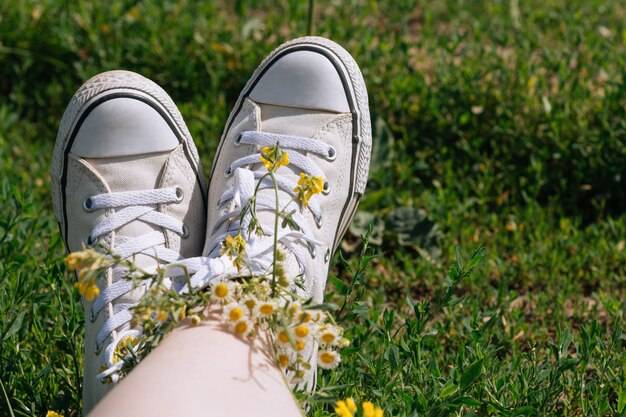 Белые кроссовки на ногах девушки на траве в солнечный летний день