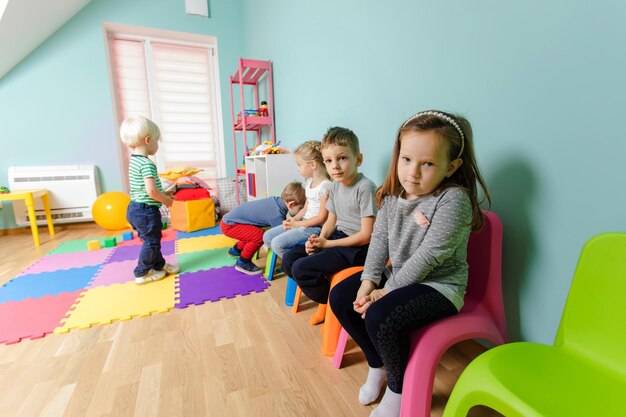 Дети сидят на разноцветных стульях в детском саду дети ждут урока