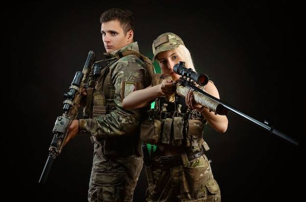 Девушка и парень в военной форме позируют со страйкбольным пистолетом на темном фоне